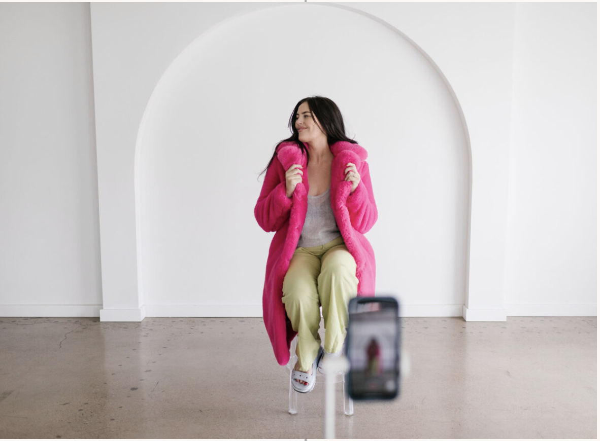 Member filming content in a bright studio wearing a pink coat